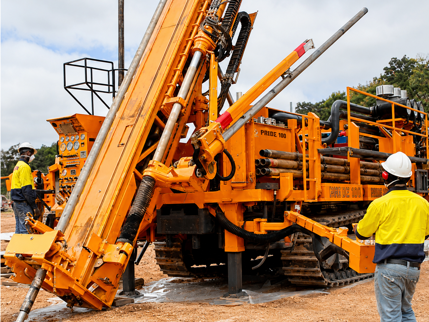 Two GTS drilling operators working safely around an orange Pride 100 drill rig